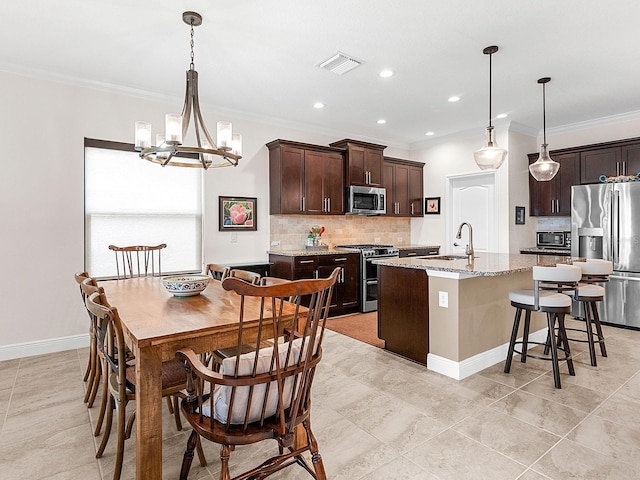 kitchen with sink, light stone countertops, an island with sink, appliances with stainless steel finishes, and dark brown cabinetry