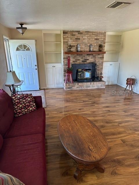 living room featuring wood-type flooring, a textured ceiling, built in features, and a wood stove