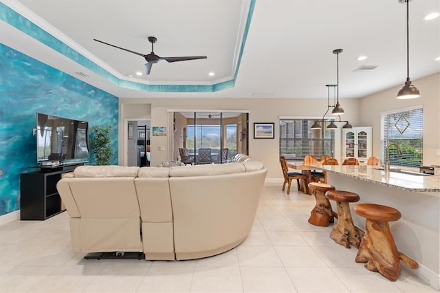 living room featuring crown molding, sink, ceiling fan, light tile patterned floors, and a tray ceiling