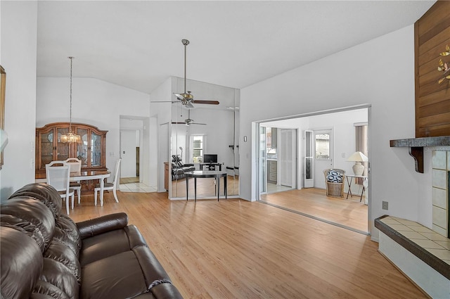 living room featuring light hardwood / wood-style floors, a baseboard heating unit, high vaulted ceiling, ceiling fan with notable chandelier, and a tile fireplace