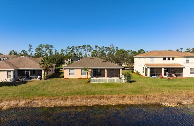 back of property with a sunroom, a water view, and a lawn