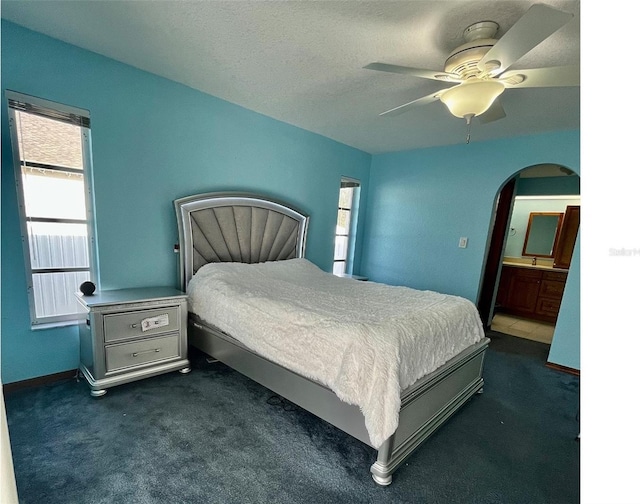 bedroom with multiple windows, ceiling fan, ensuite bath, and dark colored carpet