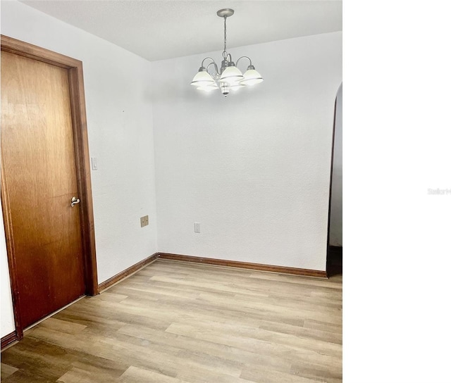 empty room featuring a chandelier and light hardwood / wood-style floors