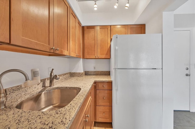 kitchen featuring light stone countertops, sink, white fridge, and track lighting