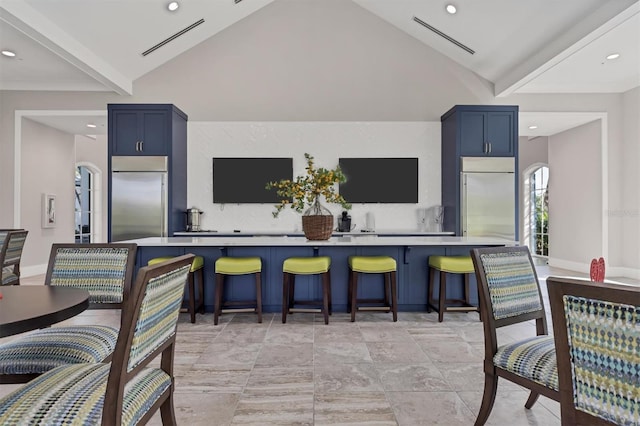 kitchen with vaulted ceiling, blue cabinets, stainless steel built in refrigerator, and a kitchen bar