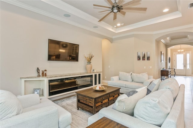 living room with french doors, crown molding, ceiling fan with notable chandelier, and a raised ceiling