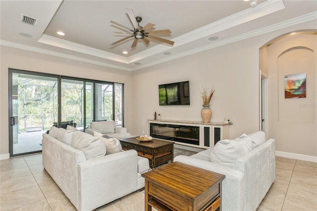 tiled living room with a raised ceiling, ceiling fan, and ornamental molding