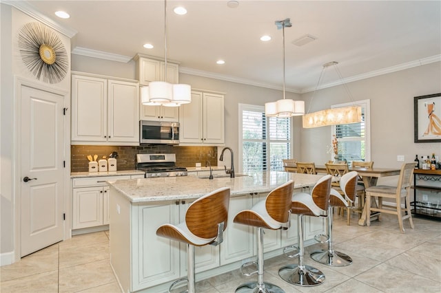 kitchen with sink, hanging light fixtures, a kitchen island with sink, light stone countertops, and stainless steel appliances