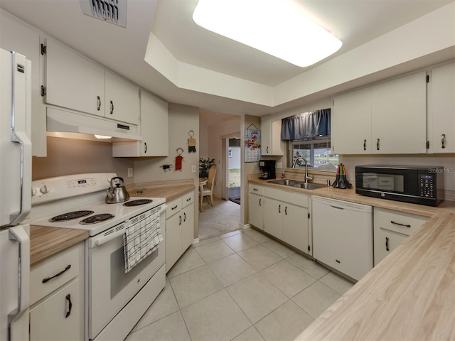 kitchen featuring light tile patterned floors, white cabinetry, a tray ceiling, white appliances, and sink