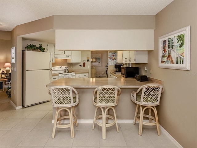 kitchen featuring white appliances, a textured ceiling, a kitchen breakfast bar, kitchen peninsula, and light tile patterned floors