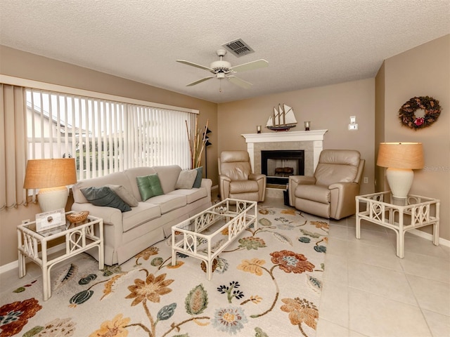 tiled living room with a textured ceiling, ceiling fan, and a fireplace