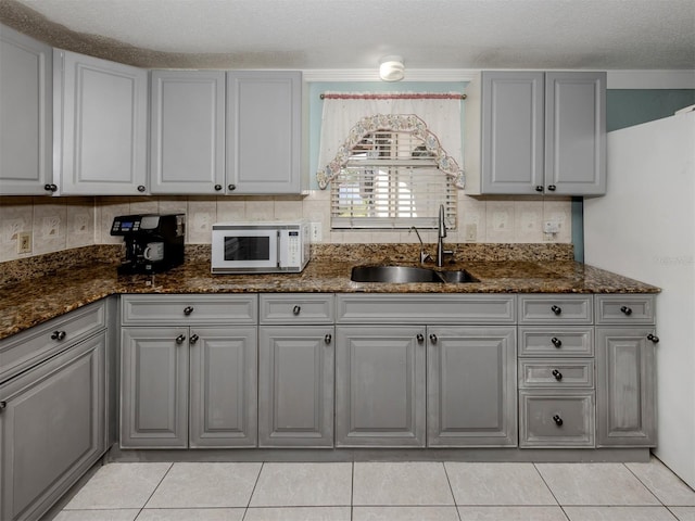 kitchen featuring dark stone counters, a textured ceiling, gray cabinetry, and sink