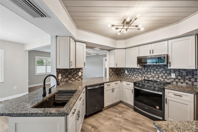 kitchen with kitchen peninsula, stainless steel appliances, sink, dark stone countertops, and white cabinetry