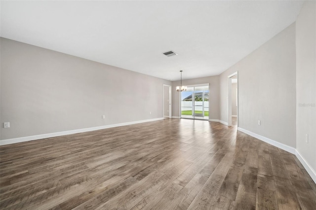 empty room featuring dark wood-type flooring and an inviting chandelier