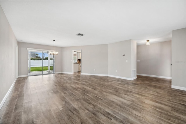 empty room with dark hardwood / wood-style flooring and a notable chandelier