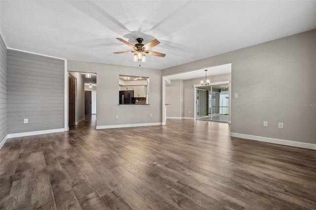 unfurnished living room featuring wooden walls, dark wood-type flooring, and ceiling fan with notable chandelier