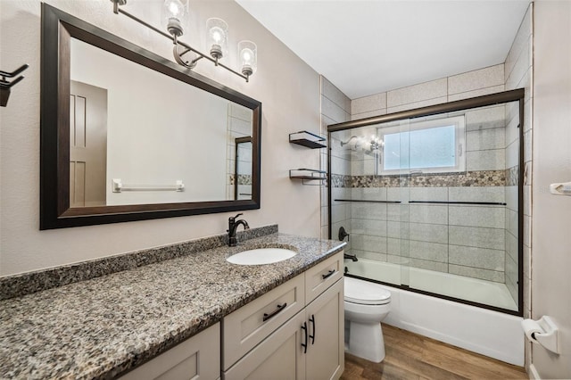 full bathroom with vanity, toilet, wood-type flooring, and bath / shower combo with glass door