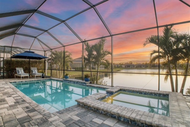 pool at dusk with a water view, an in ground hot tub, a patio area, and glass enclosure