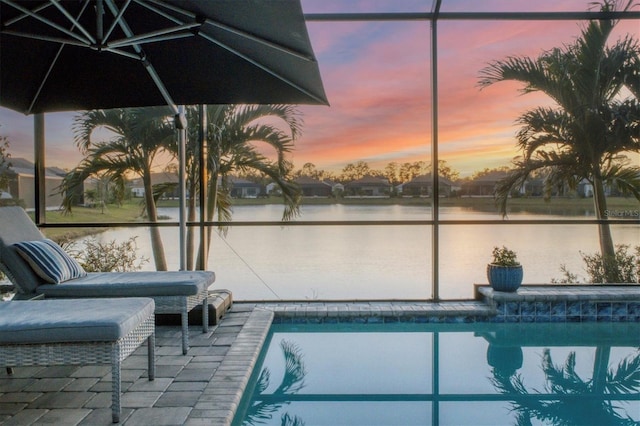 pool at dusk with a patio, a water view, and a lanai