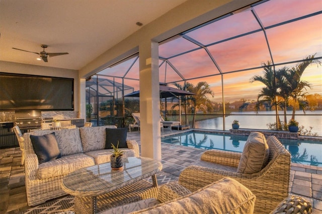 pool at dusk with ceiling fan, outdoor lounge area, a water view, a patio area, and an outdoor kitchen