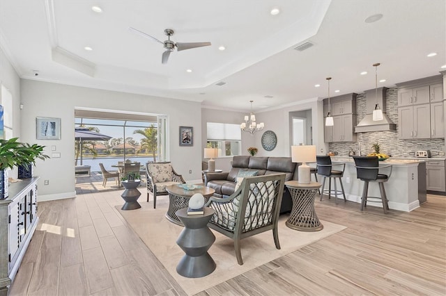 living room featuring light hardwood / wood-style floors, ceiling fan with notable chandelier, ornamental molding, and a raised ceiling