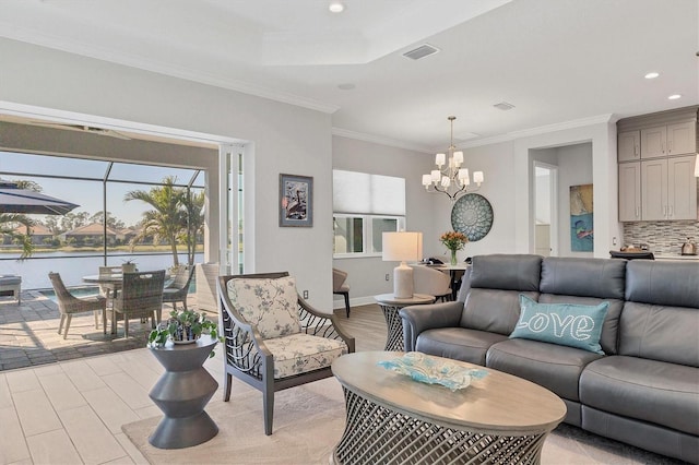 living room with a raised ceiling, ornamental molding, a water view, and an inviting chandelier