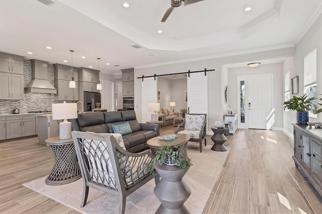 living room with crown molding, a tray ceiling, a barn door, and ceiling fan