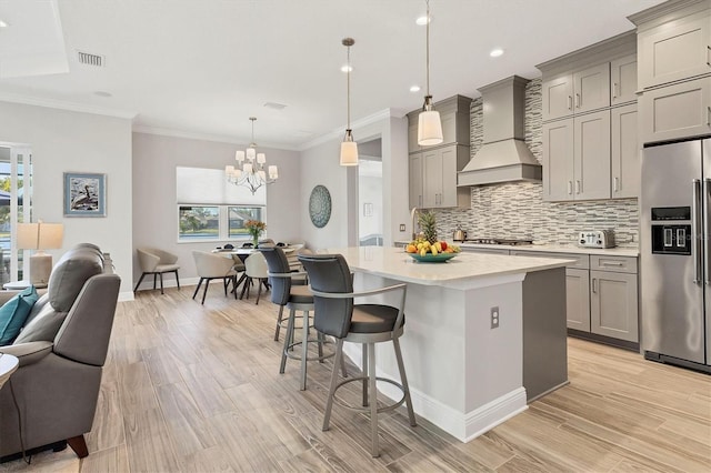 kitchen featuring a breakfast bar, custom exhaust hood, appliances with stainless steel finishes, a kitchen island, and pendant lighting