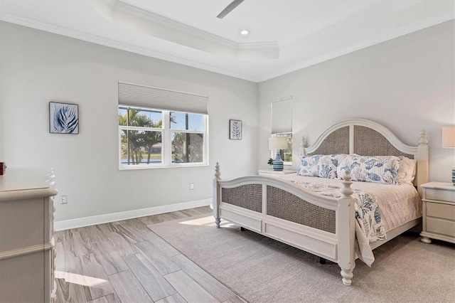 bedroom featuring crown molding, light wood-type flooring, ceiling fan, and a tray ceiling