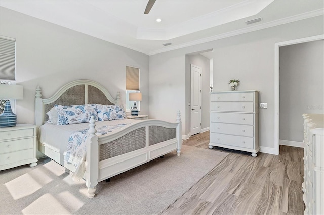 bedroom featuring ceiling fan, ornamental molding, a tray ceiling, and light hardwood / wood-style flooring