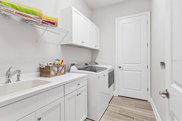 clothes washing area with separate washer and dryer, sink, and cabinets