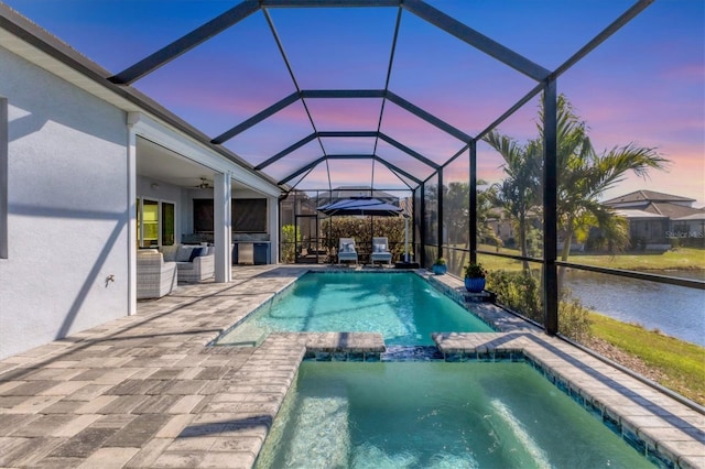 pool at dusk featuring ceiling fan, outdoor lounge area, glass enclosure, a patio area, and an in ground hot tub