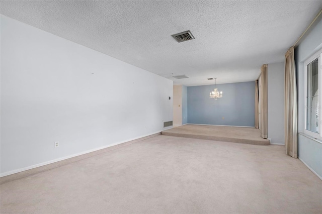 unfurnished room with light colored carpet, a textured ceiling, and a notable chandelier