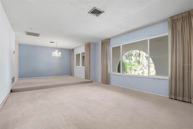 spare room featuring a chandelier, a textured ceiling, and light colored carpet