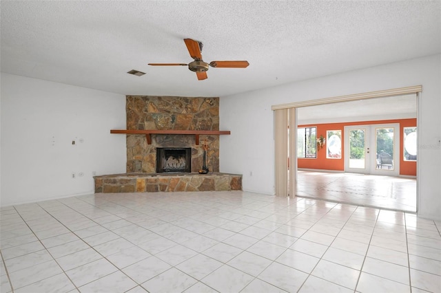 unfurnished living room featuring ceiling fan, french doors, a stone fireplace, a textured ceiling, and light tile patterned floors