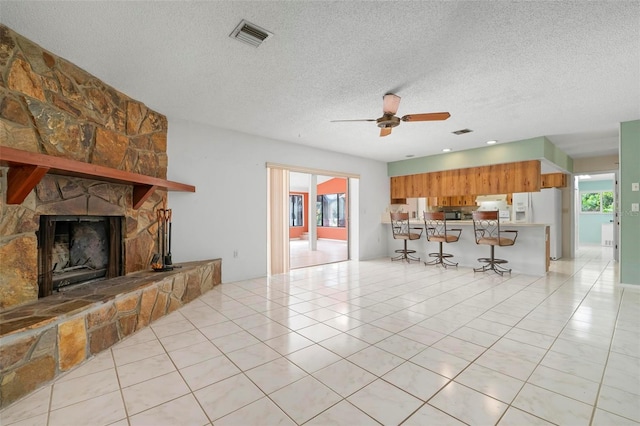 unfurnished living room featuring light tile patterned floors, a textured ceiling, a stone fireplace, and ceiling fan