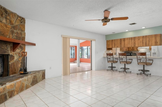 kitchen featuring a stone fireplace, ceiling fan, white fridge with ice dispenser, a textured ceiling, and a breakfast bar area