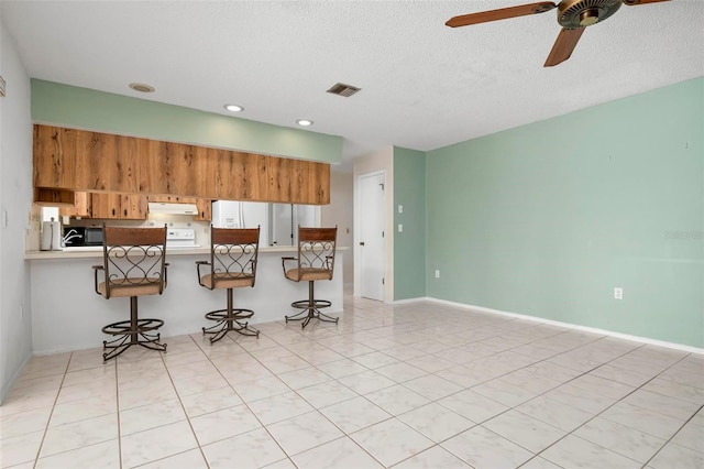 kitchen with a kitchen breakfast bar, kitchen peninsula, light tile patterned floors, and a textured ceiling