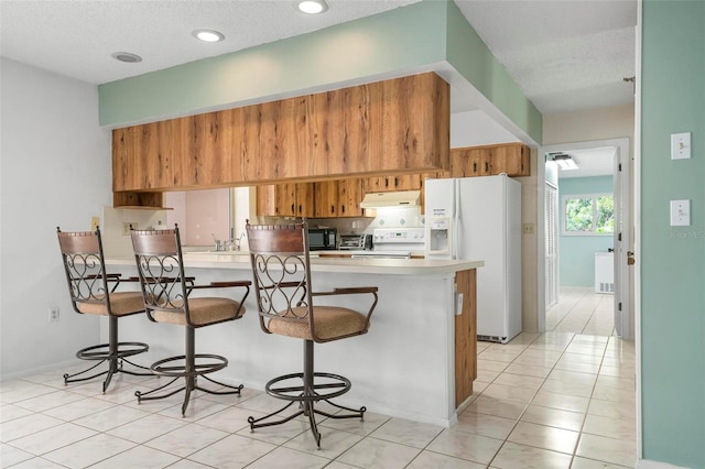 kitchen featuring white appliances, a textured ceiling, light tile patterned flooring, a kitchen bar, and kitchen peninsula