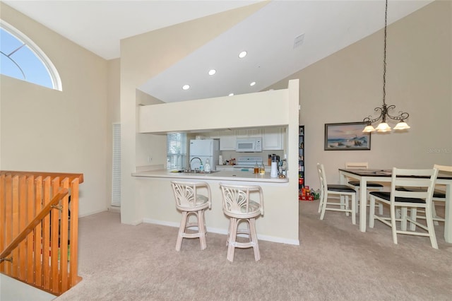 kitchen with white appliances, an inviting chandelier, decorative light fixtures, light colored carpet, and kitchen peninsula