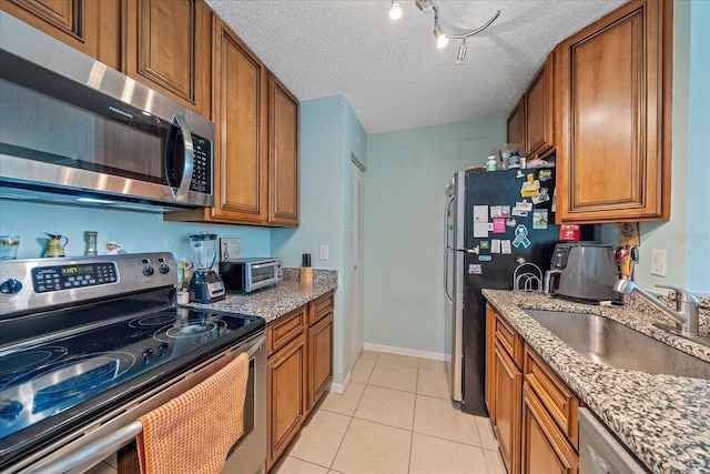 kitchen with sink, stainless steel appliances, a textured ceiling, light tile patterned floors, and light stone counters