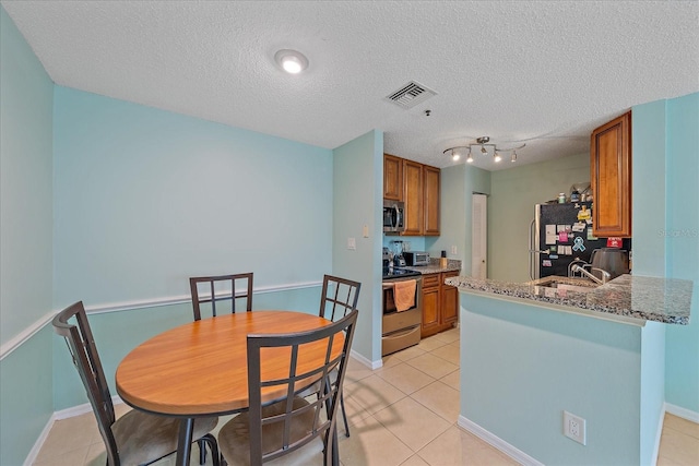 kitchen featuring sink, stainless steel appliances, a textured ceiling, light tile patterned floors, and stone countertops