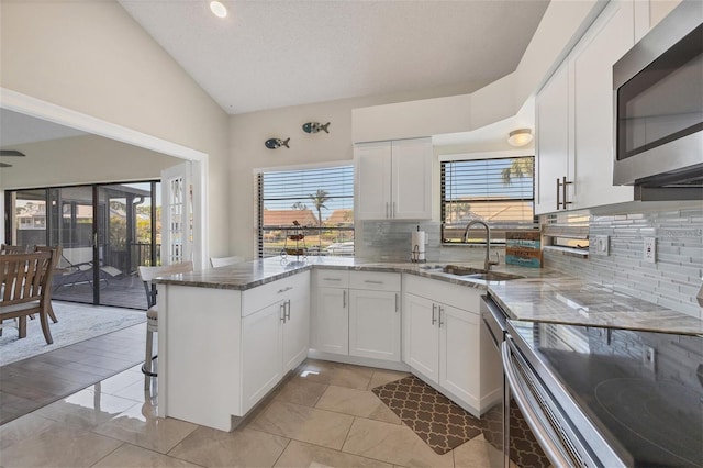 kitchen featuring kitchen peninsula, appliances with stainless steel finishes, vaulted ceiling, sink, and white cabinets