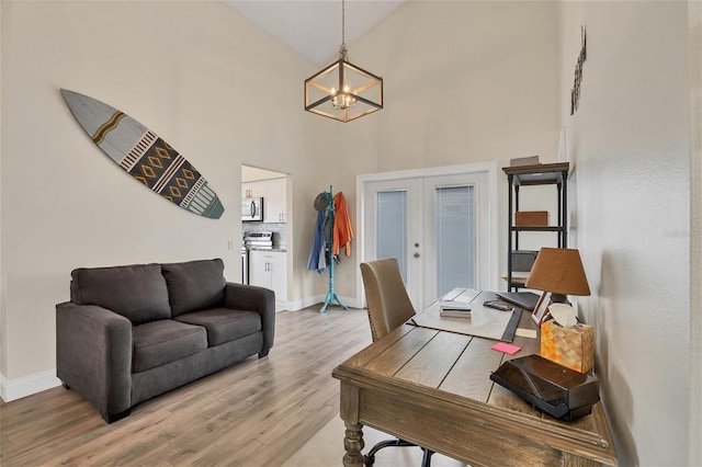 office space with french doors, light wood-type flooring, high vaulted ceiling, and an inviting chandelier