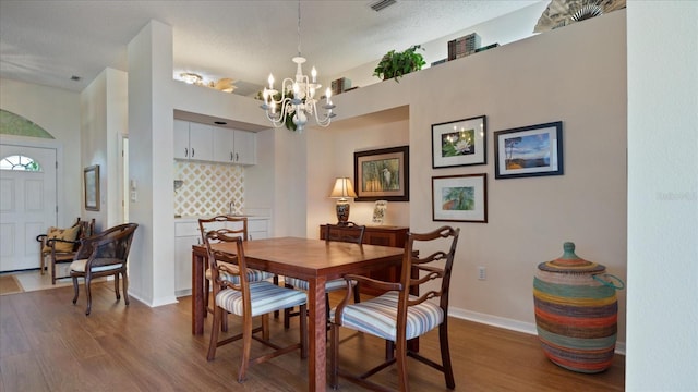 dining area with wood-type flooring, a textured ceiling, and an inviting chandelier