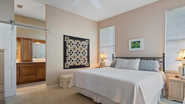 bedroom with a textured ceiling, light colored carpet, ceiling fan, a barn door, and connected bathroom