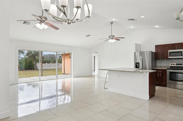 kitchen with appliances with stainless steel finishes, decorative light fixtures, lofted ceiling, a center island, and light stone countertops