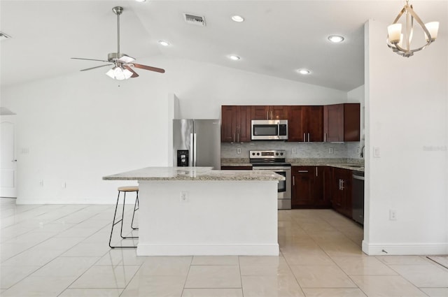 kitchen with tasteful backsplash, light stone counters, decorative light fixtures, a kitchen island, and stainless steel appliances