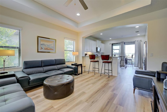living room with ceiling fan, a raised ceiling, and light hardwood / wood-style floors