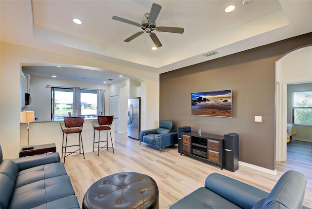 living room with a tray ceiling, ceiling fan, and light wood-type flooring